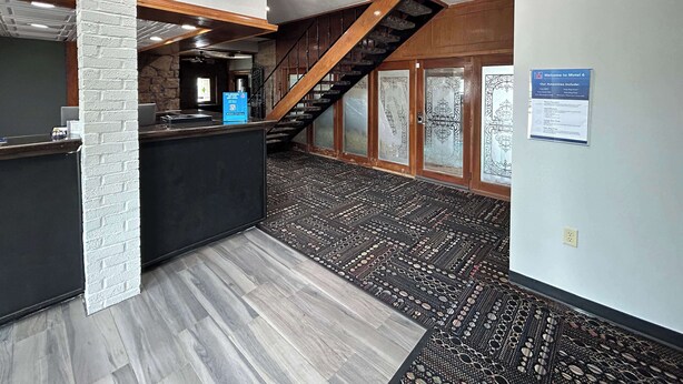 A reception area with a modern design, including a reception desk, a staircase, and a patterned carpet. - Motel 6 Ada, OK (Ada)