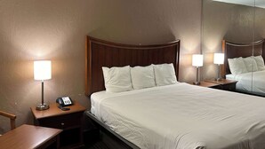 A hotel room with a large bed, two bedside tables, a desk, and a mirror. - Motel 6 Ada, OK (Ada)