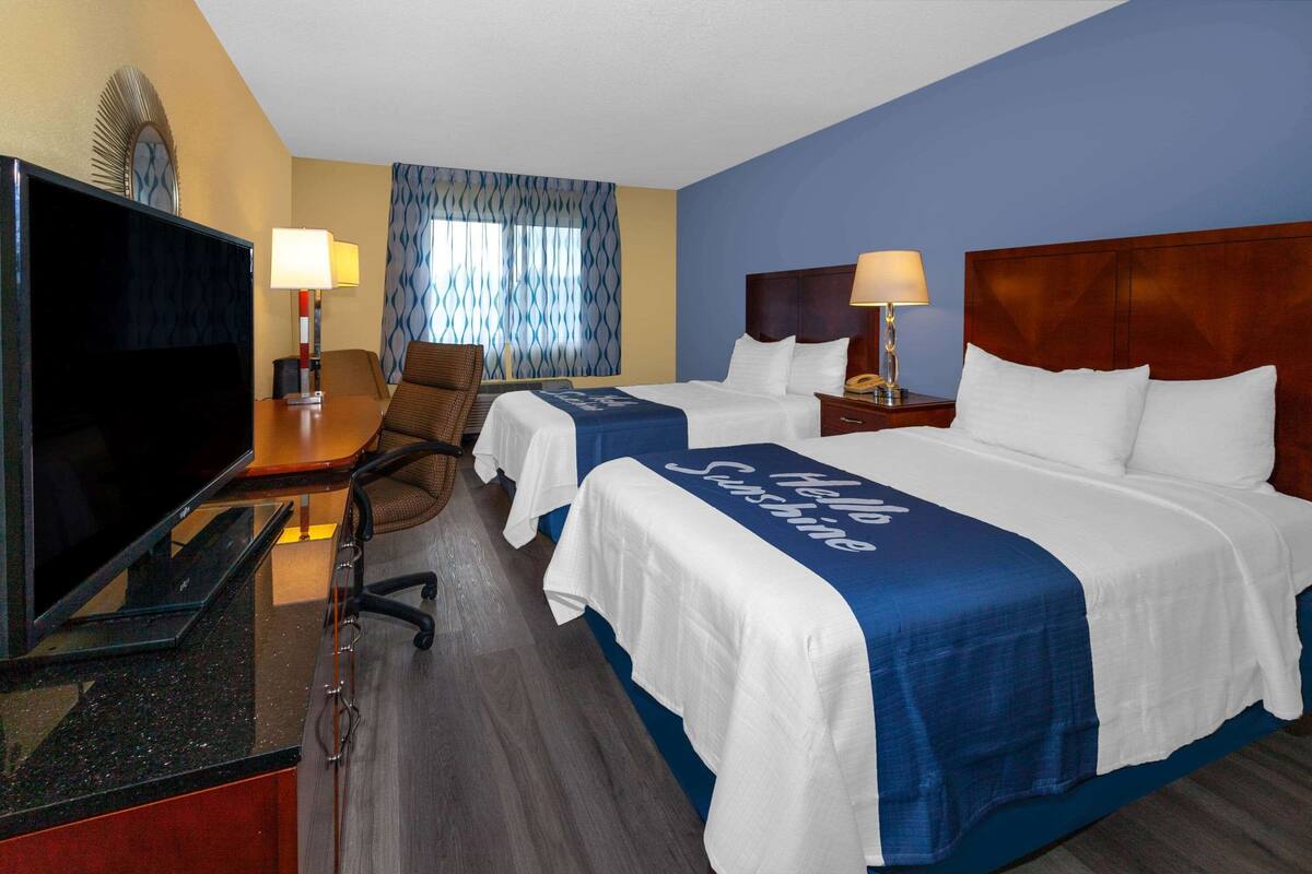A hotel room with two beds, a TV, a desk, and a chair.