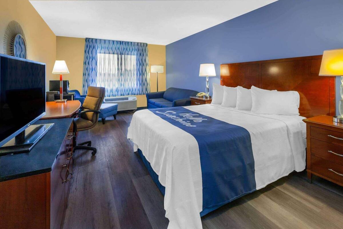 A hotel room with a bed, a desk with a TV, a chair, a sofa, and two bedside lamps.