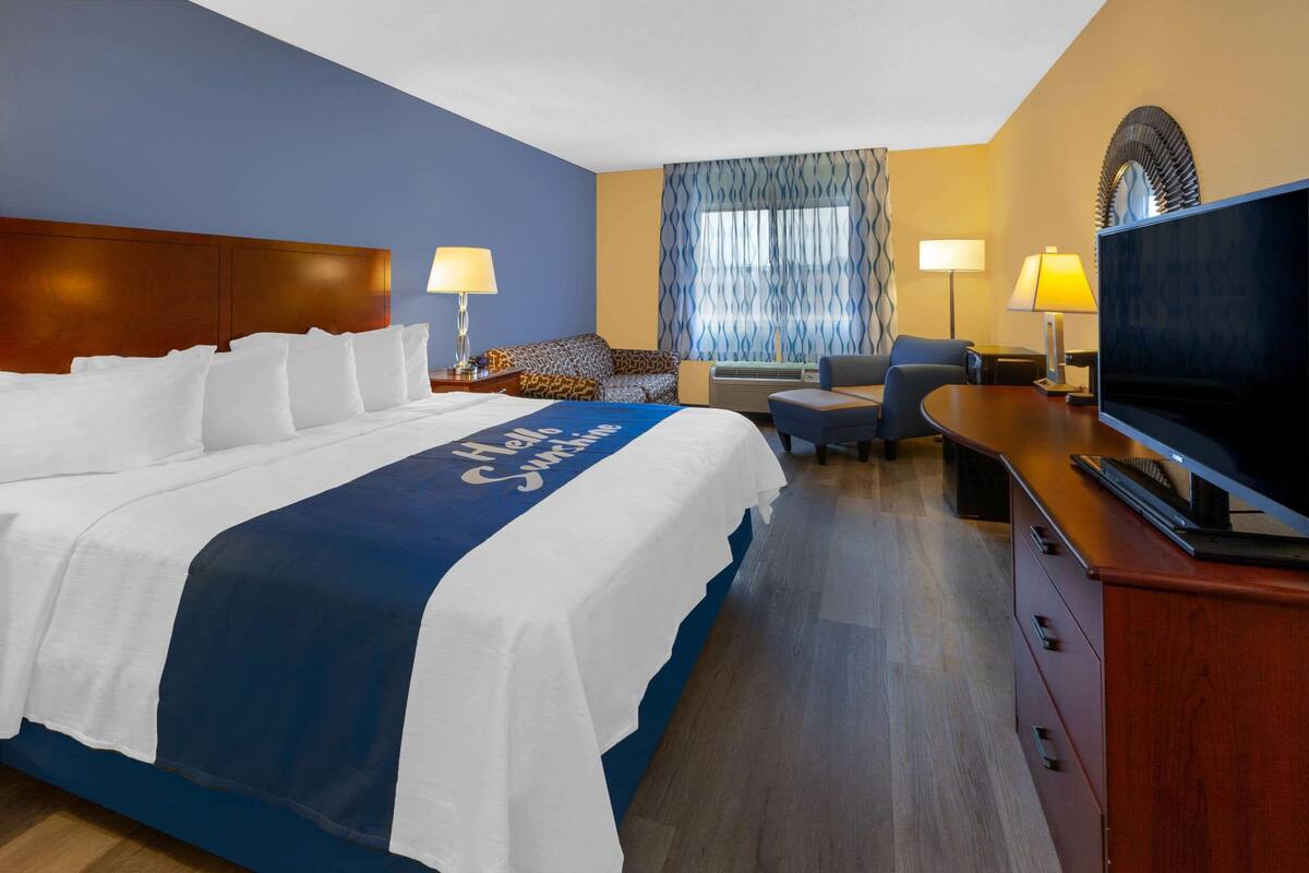 A hotel room with a large bed, a desk with a TV, a sofa, and a window with curtains.