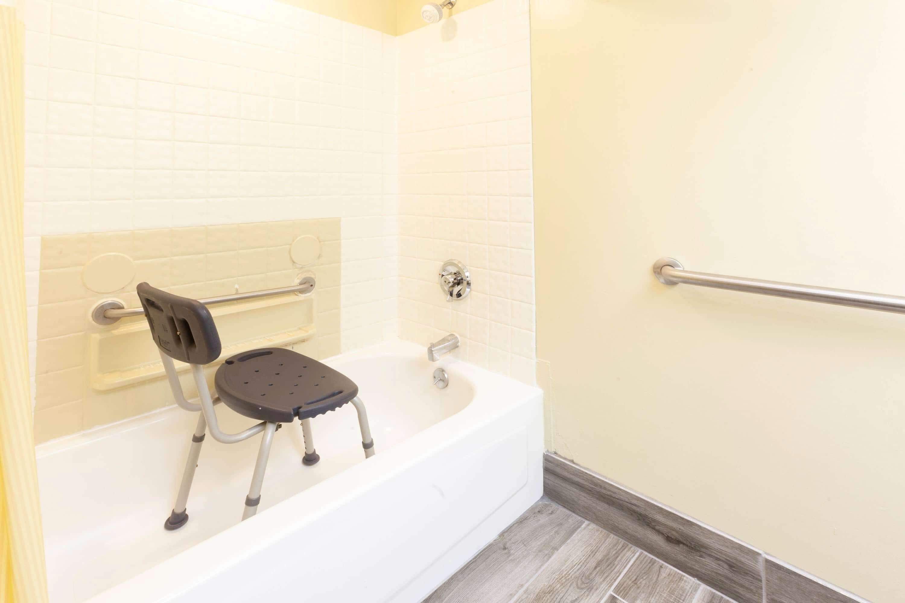 A bathroom with a bathtub, a wheelchair-accessible shower seat, and a grab bar.