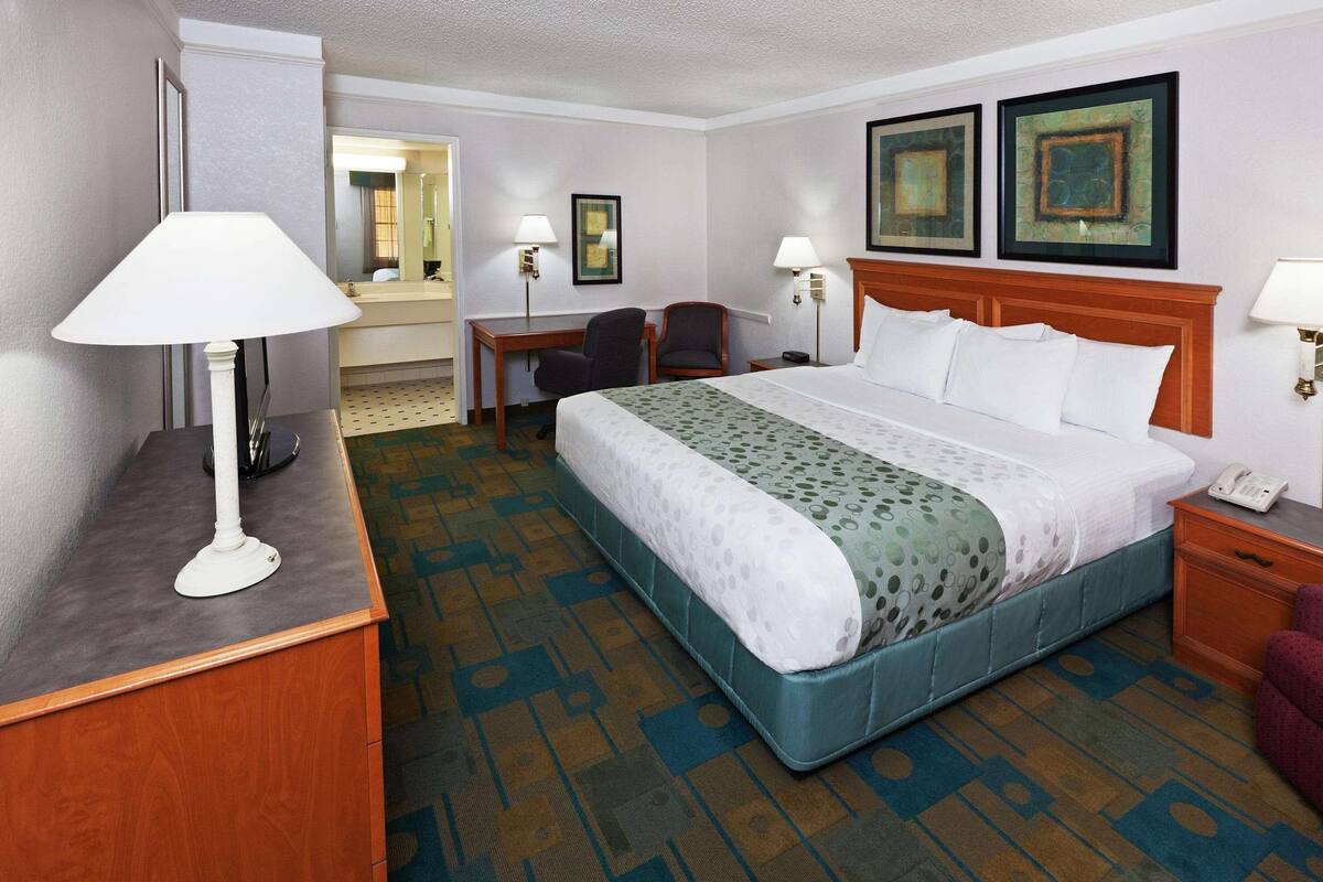 A hotel room with a bed, desk, chair, and a lamp.