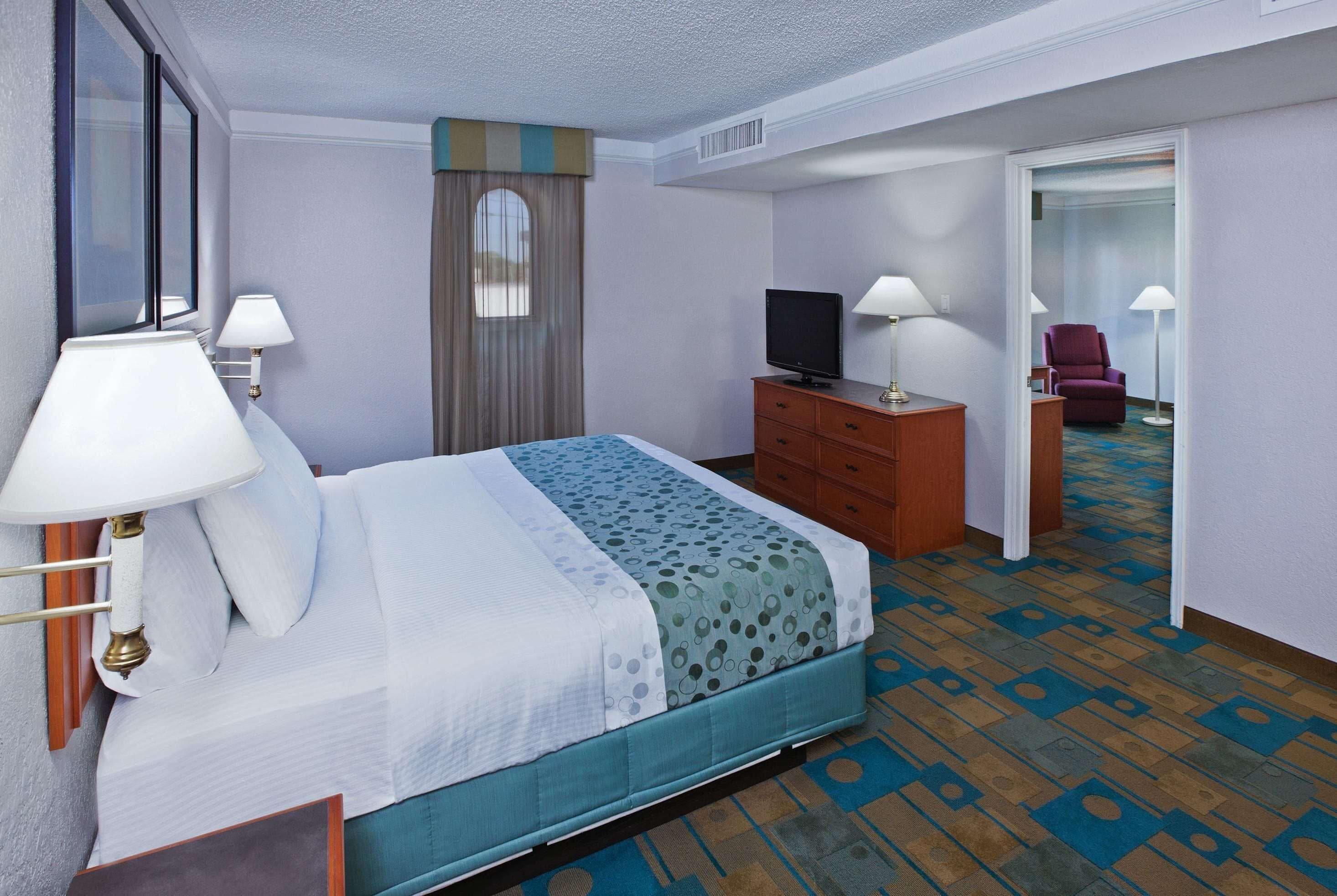 Una habitación de hotel con una cama, televisión, cómoda y una silla.