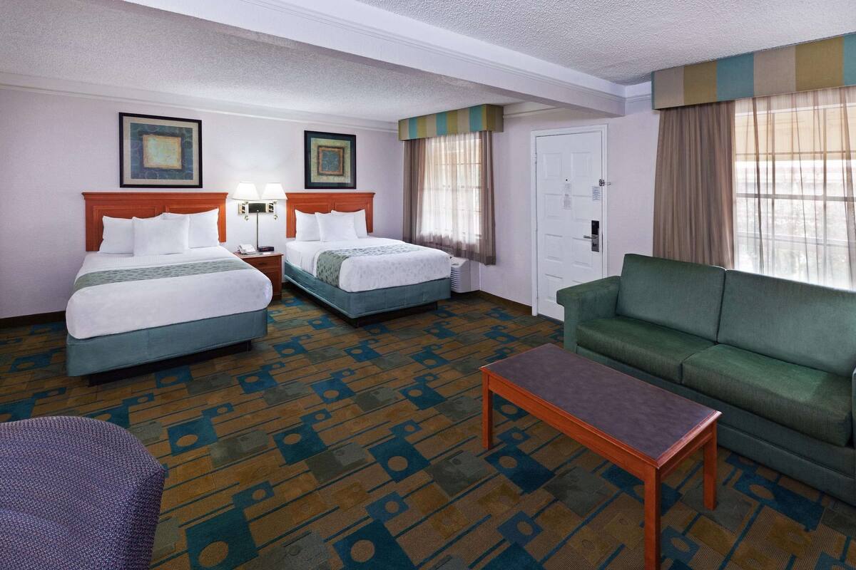A hotel room with two beds, a green sofa, a small table, and patterned carpet.