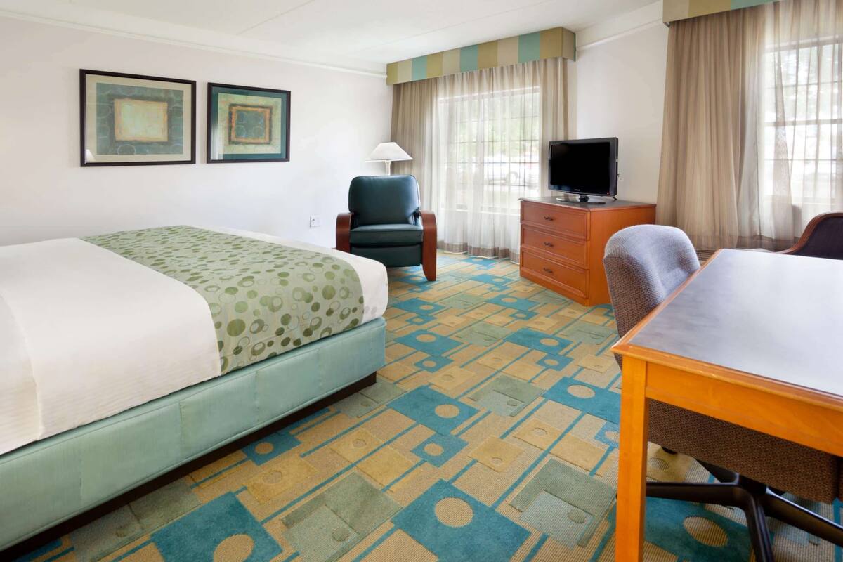 A hotel room with a bed, a desk, a chair, a television, and two framed pictures on the wall.