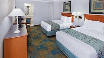 A hotel room with two beds, a desk, a chair, a lamp, and a mirror.