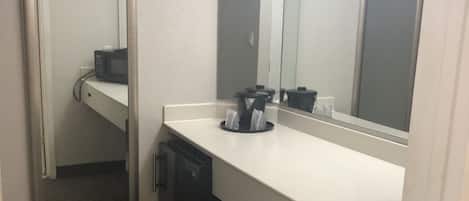 A hotel bathroom with a white sink, a mirror, a microwave, and a trash bin.