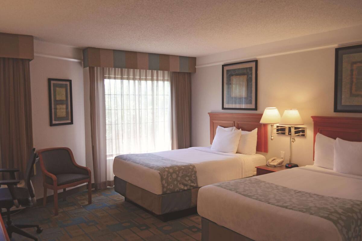 A hotel room with two beds, a desk, a chair, and a window with curtains.