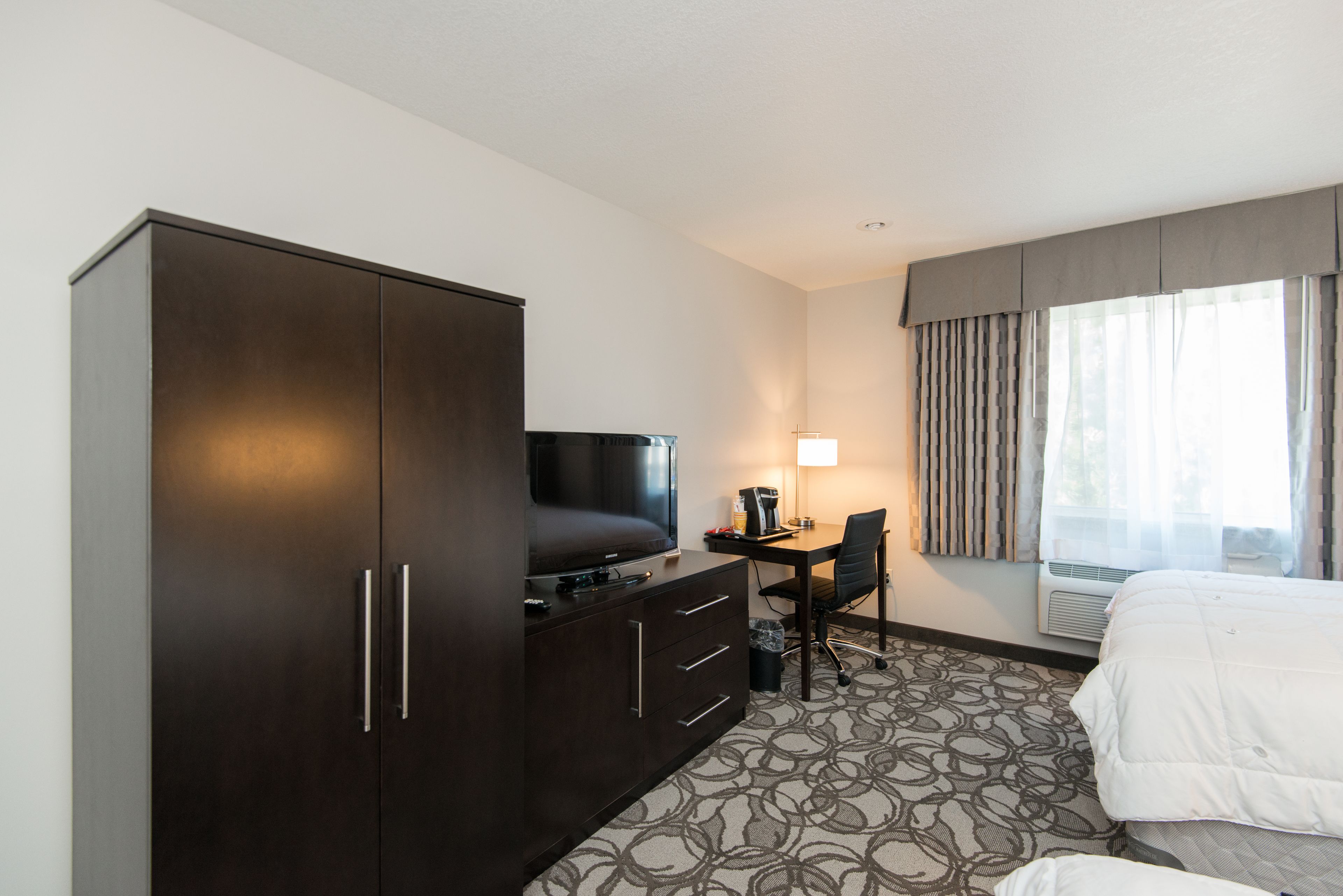 Quarto de hotel com guarda-roupa espaçoso, televisão de tela plana, escrivaninha com luminária, uma cadeira e uma cama.