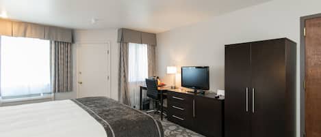A hotel room with a bed, a desk with a computer, a television, and a wardrobe.