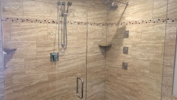 A glass-enclosed shower with multiple showerheads and a handheld shower attachment.