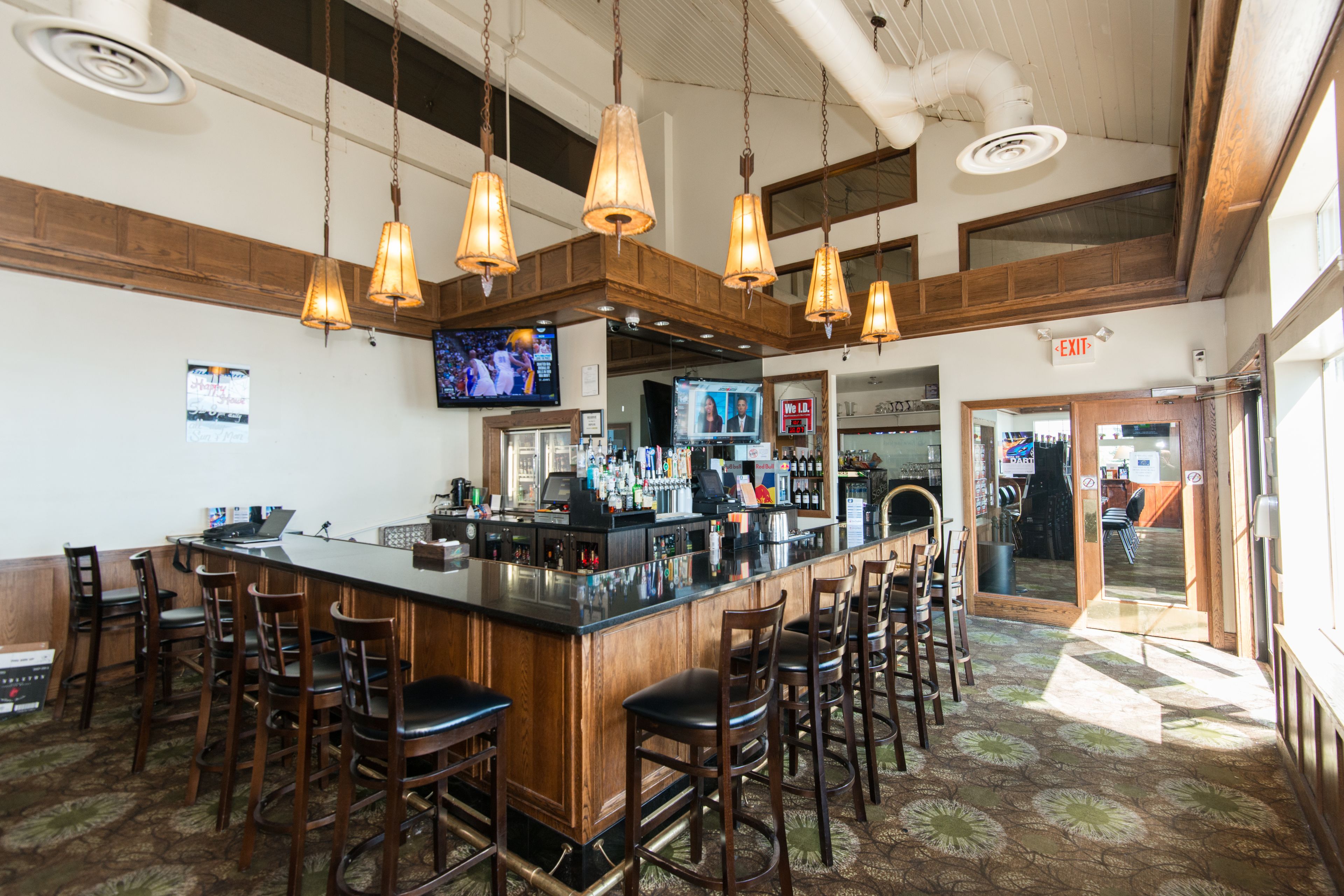 Uma área de bar com um balcão comprido, vários bancos e luminárias pendentes.