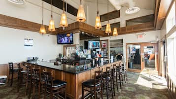 Uma área de bar com um balcão comprido, vários bancos e luminárias pendentes.