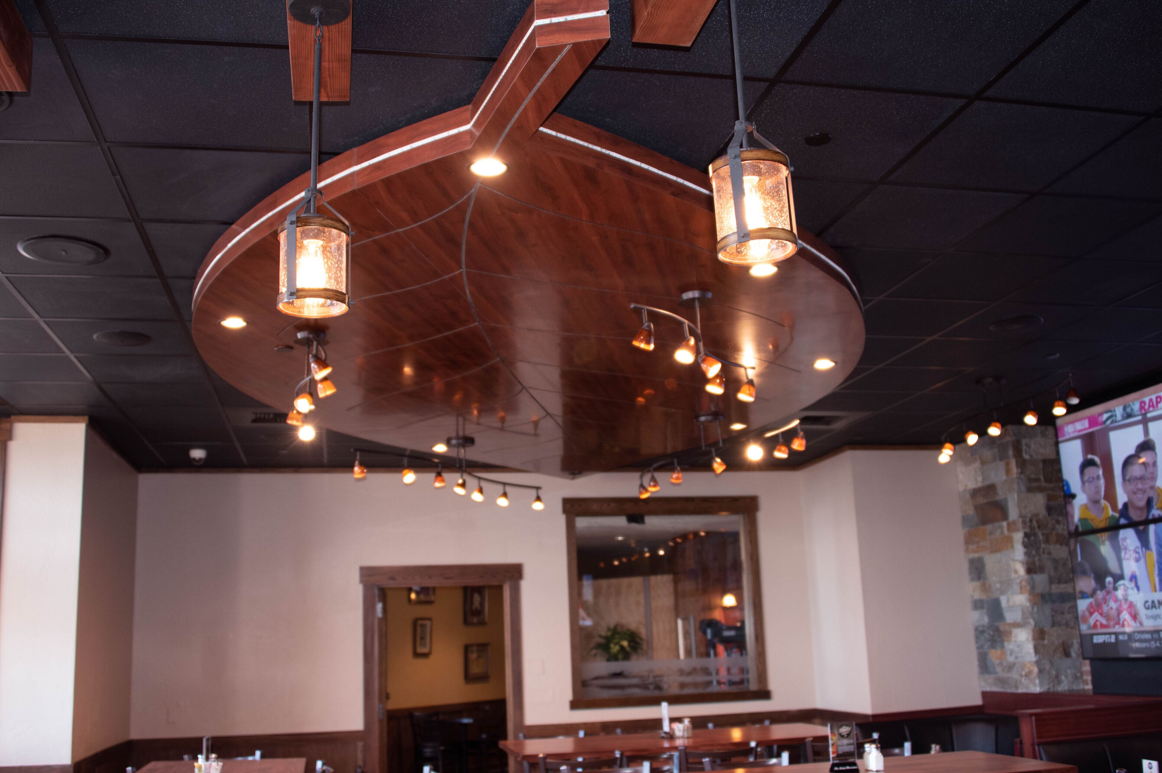 A restaurant interior with wooden ceiling beams, hanging pendant lights, and a large screen displaying a sports event.