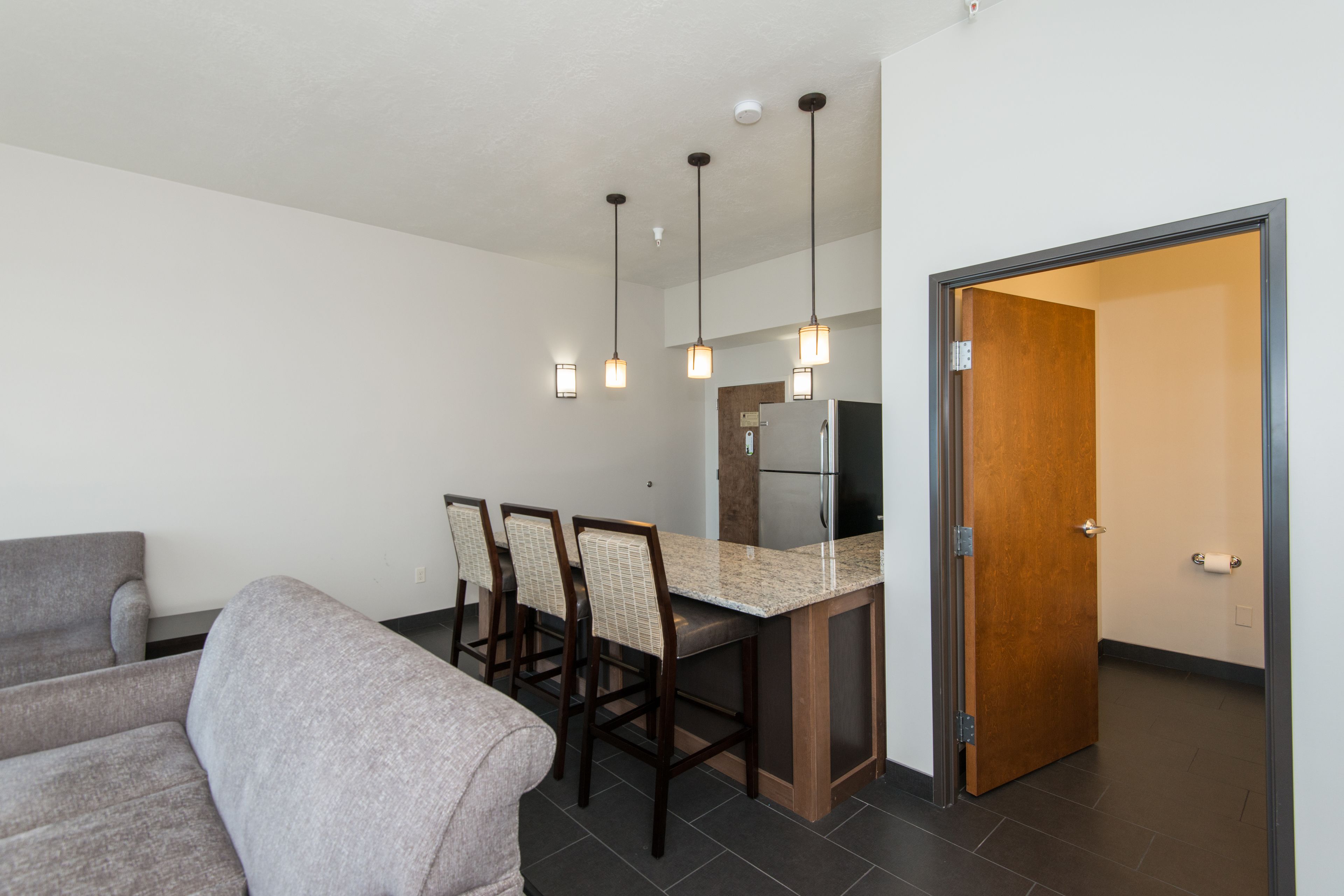 A modern kitchen with a central island, bar stools, pendant lighting, and a refrigerator.