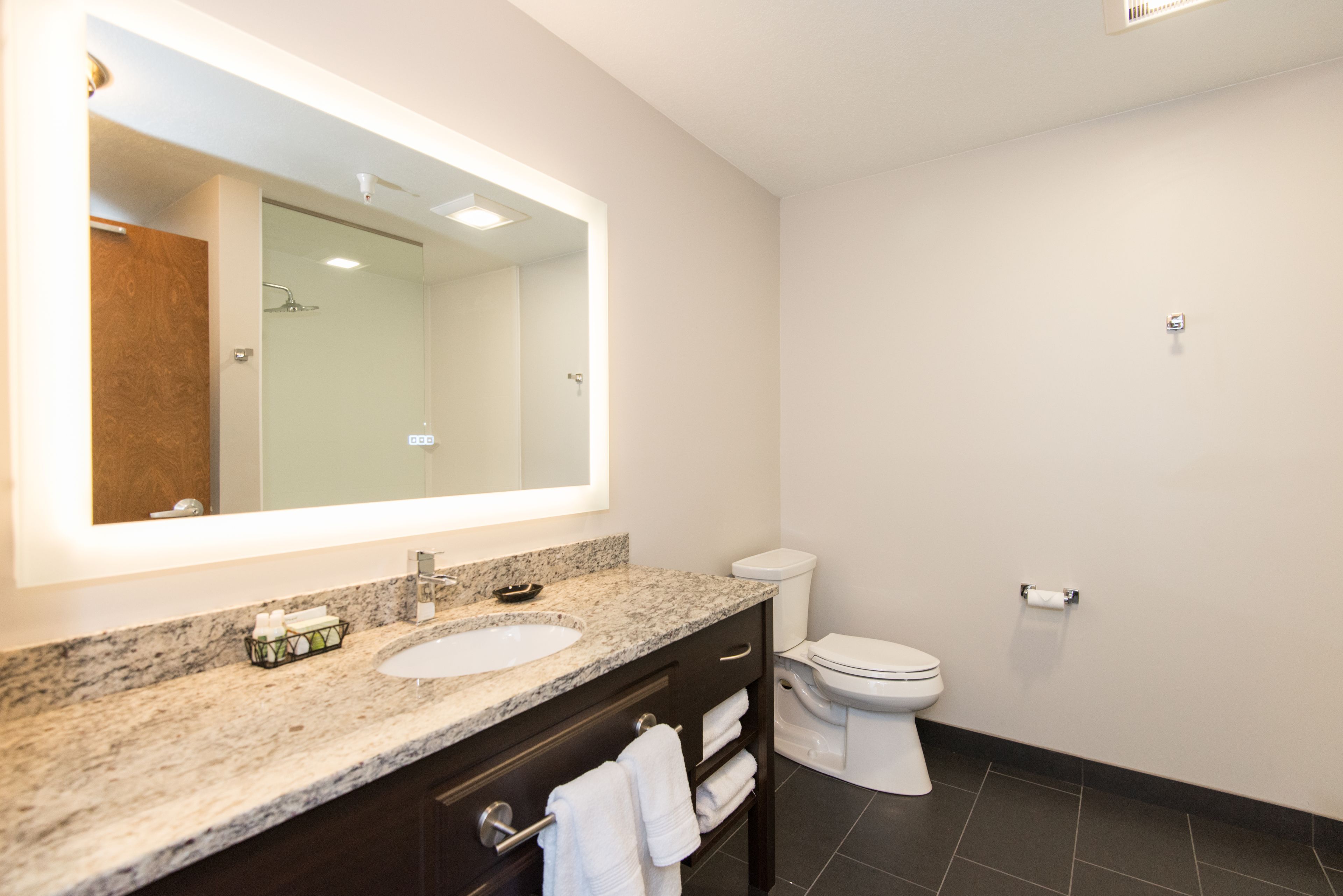 A modern bathroom with a marble sink, a large mirror, a toilet, and dark floor tiles.