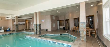 Une piscine intérieure avec un bord carrelé, un espace détente avec des tables et des chaises, et une porte de sortie bien visible.