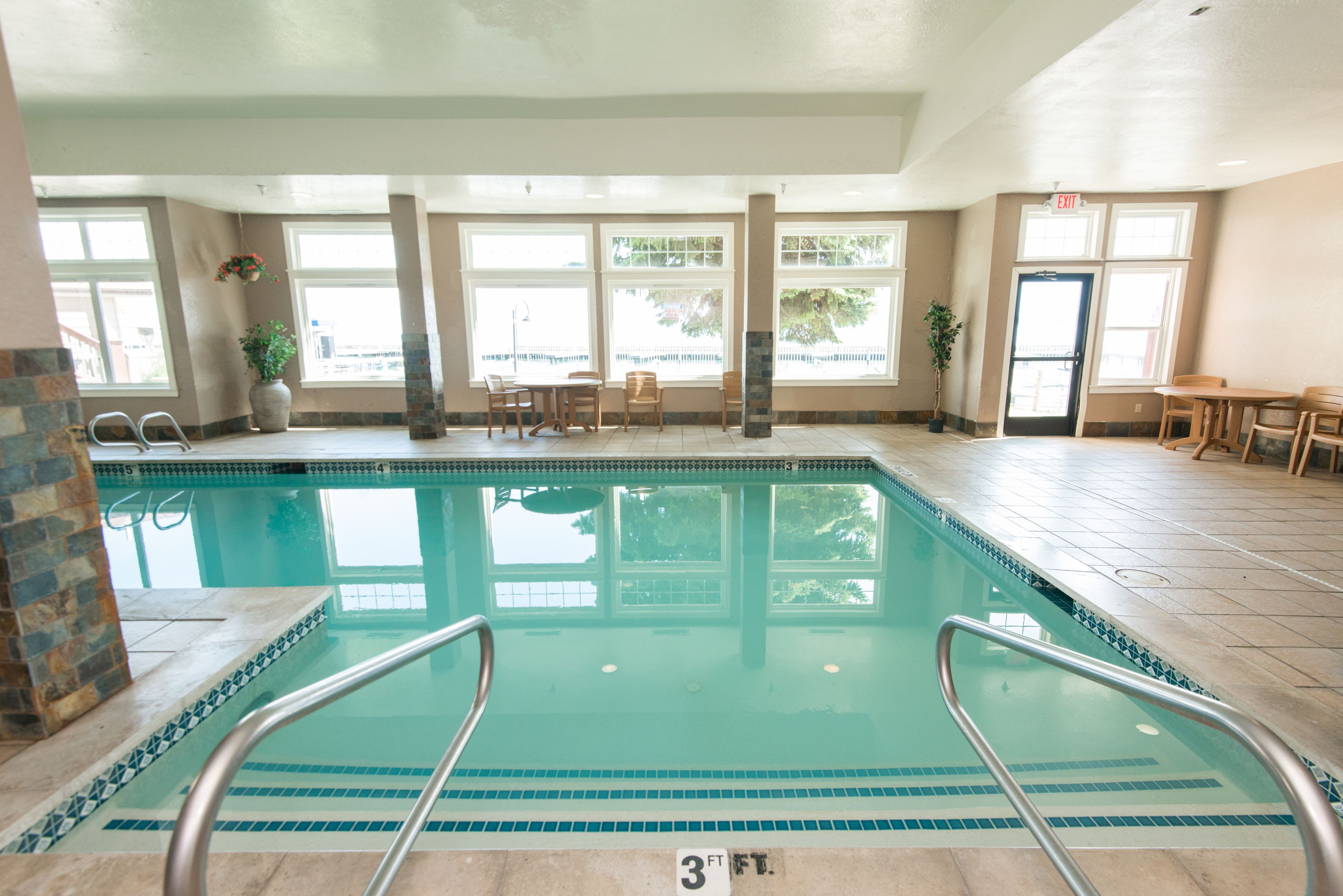 An indoor swimming pool with clear water, a 3 FT depth marker, and a view of the outdoors through large windows.