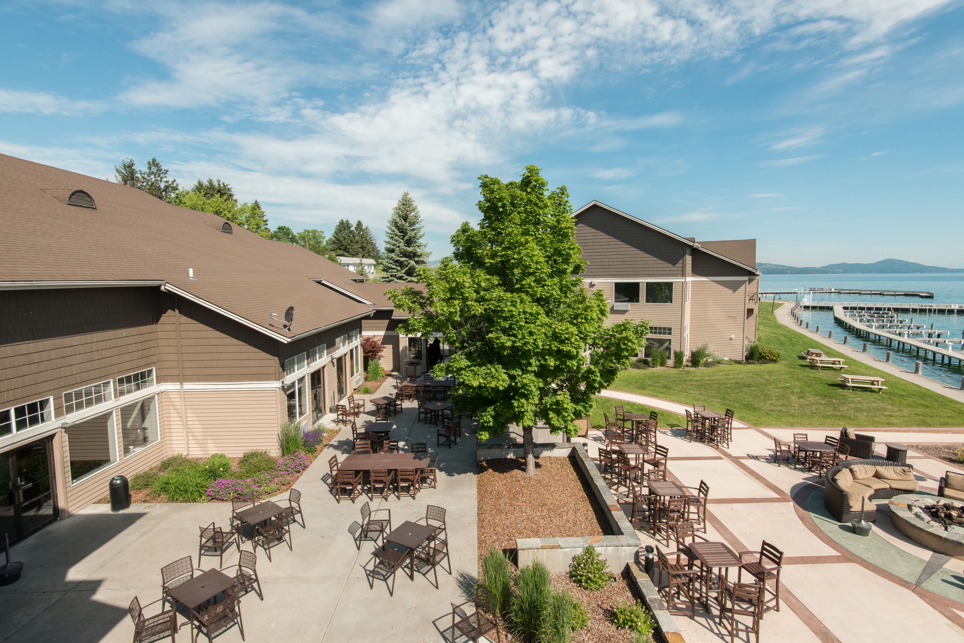 A courtyard with outdoor seating, a large tree, and a view of a body of water.