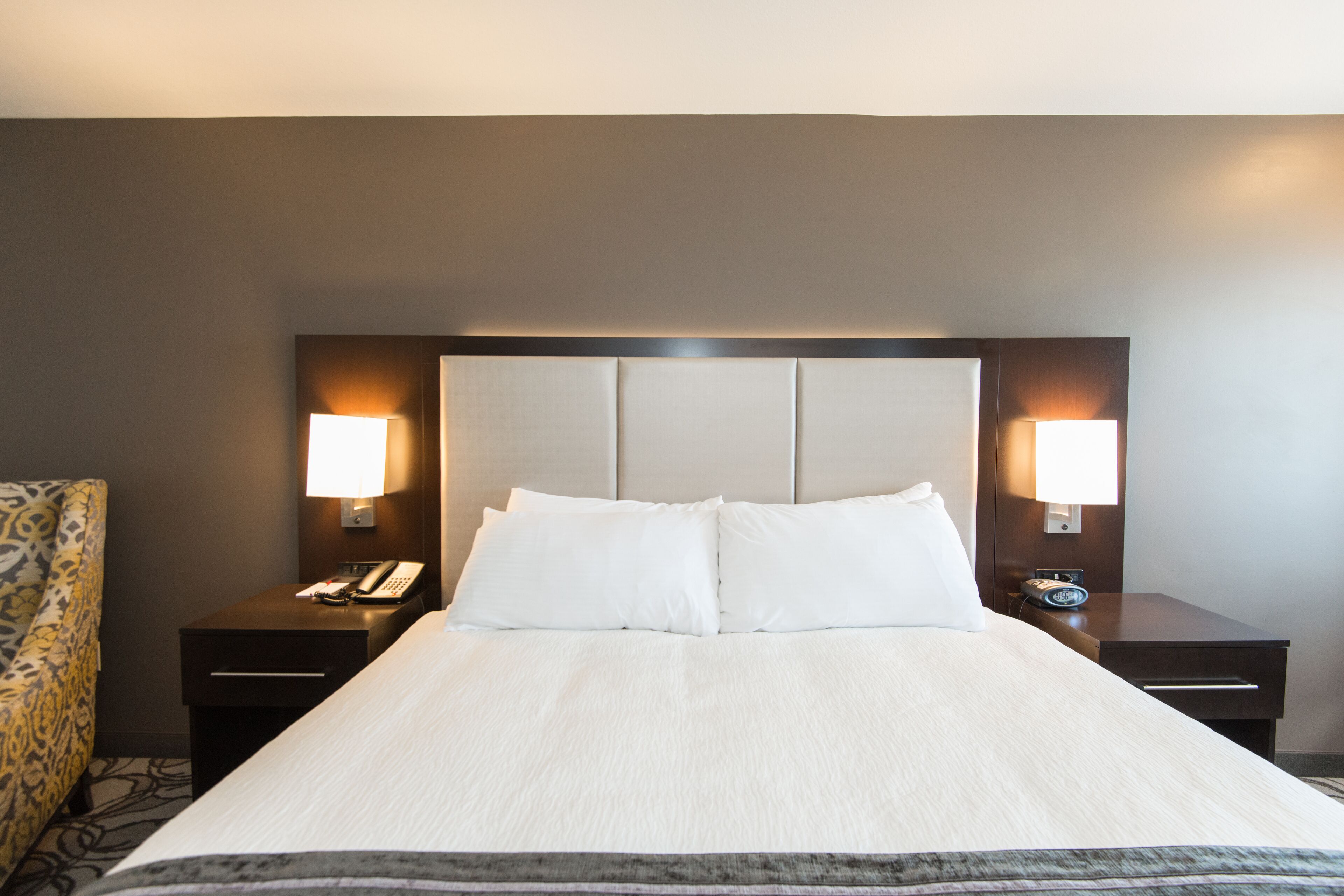 A hotel room with a large bed, two bedside tables, a chair, and wall-mounted lamps.