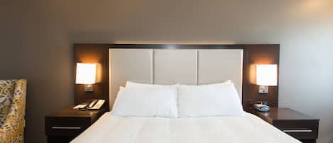 Habitación de hotel con una cama grande, dos mesitas de noche, una silla y lámparas de pared.