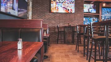 A restaurant interior with brick walls, wooden tables and chairs, and multiple televisions mounted on the wall.