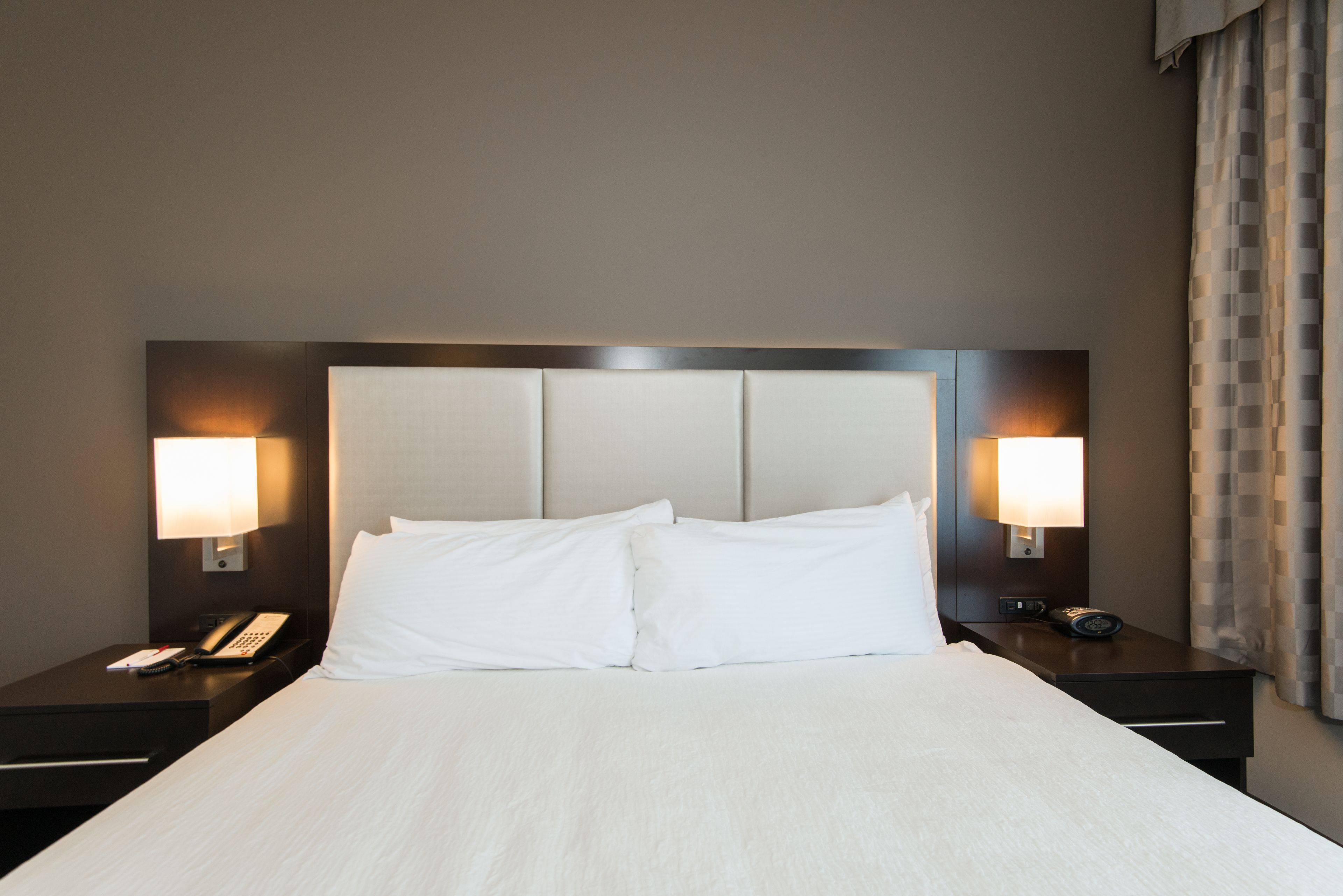 A hotel room with a large bed, two bedside tables, and two wall-mounted lamps.
