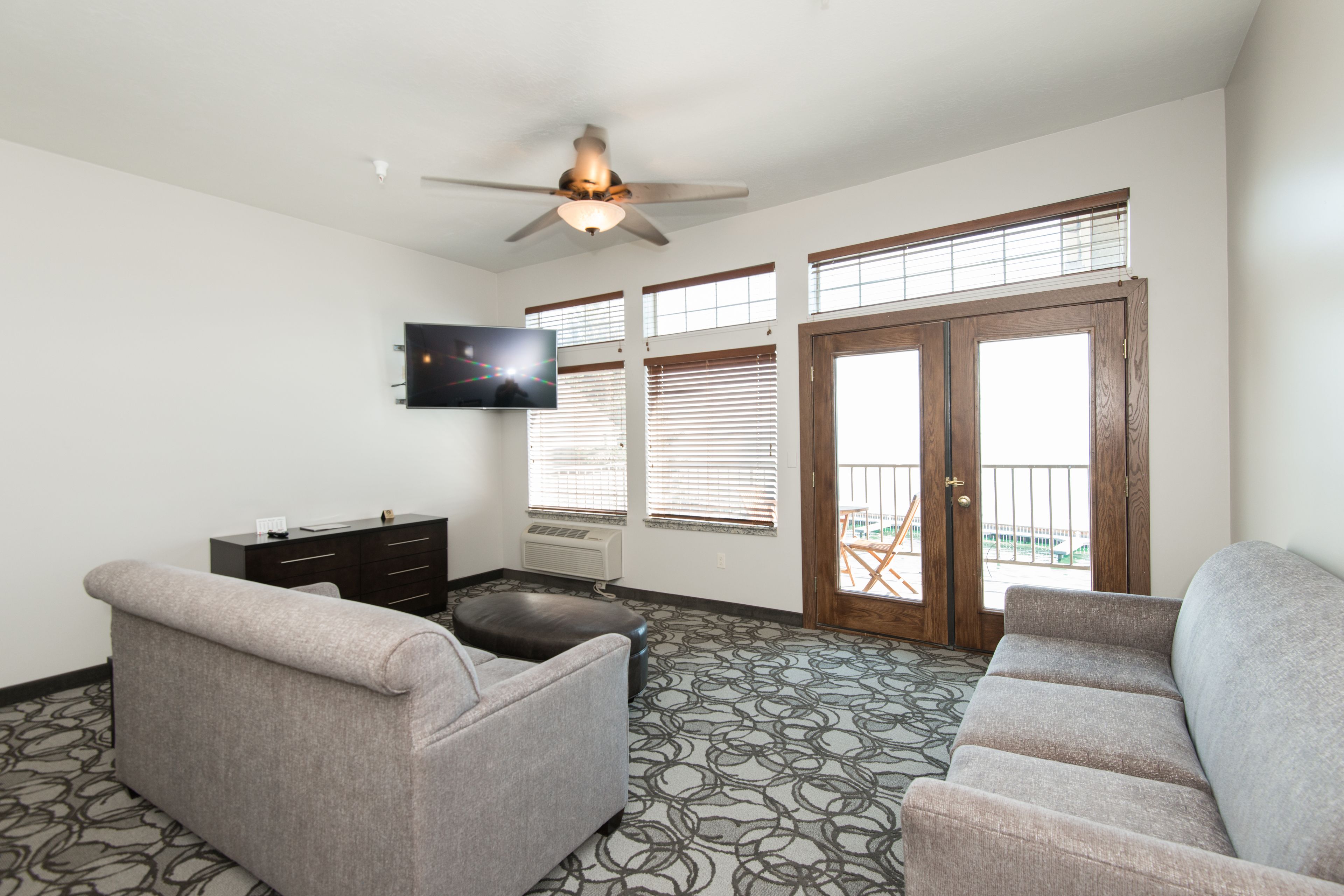 A living room with a ceiling fan, a TV mounted on the wall, a sofa, a coffee table, and a patterned carpet.