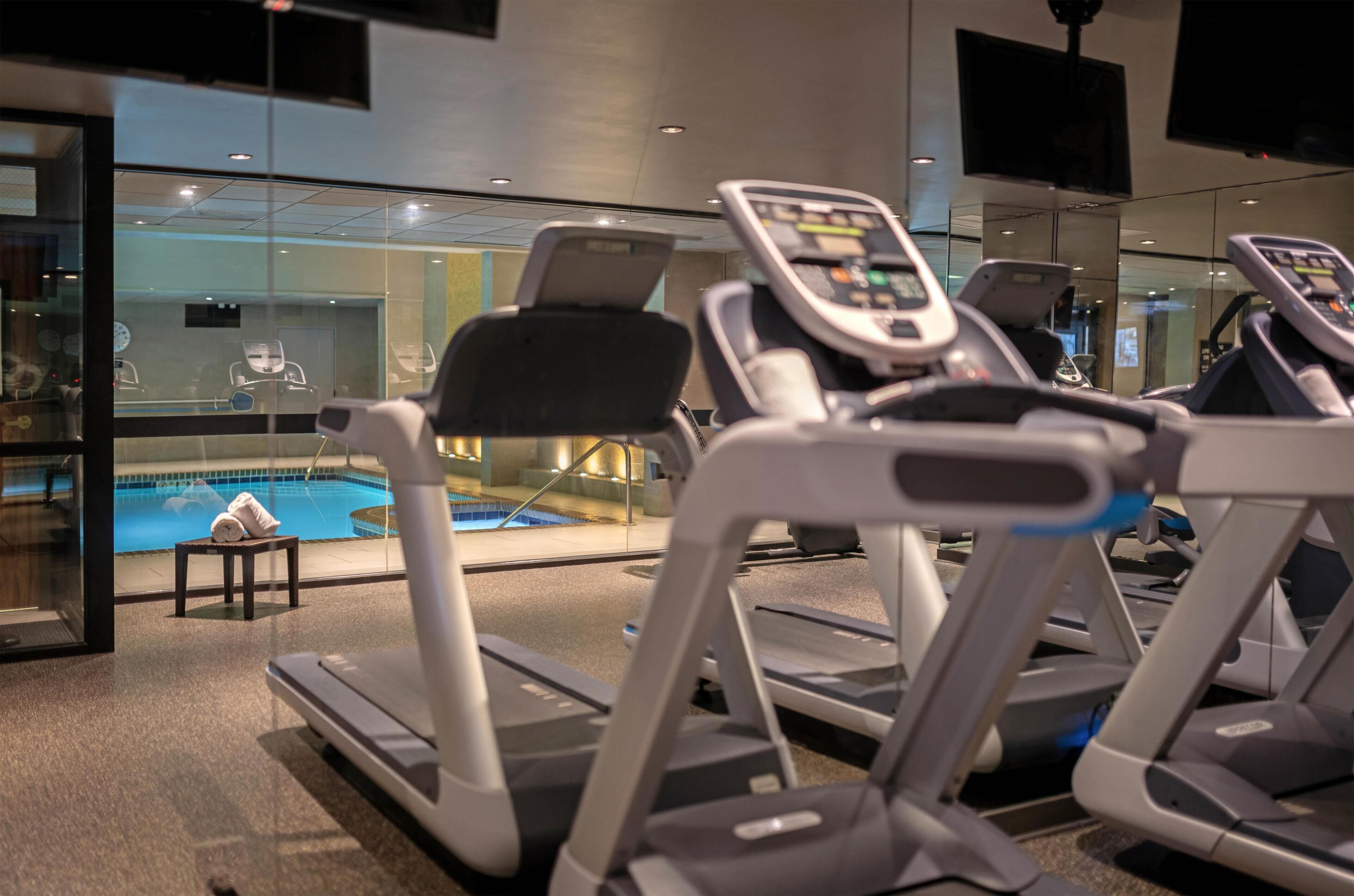 Une salle de sport équipée de tapis de course, d’une piscine et d’un miroir qui reflète l’intérieur.