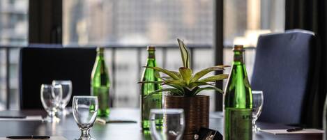 A dining table with green bottles, a potted plant, and empty wine glasses.