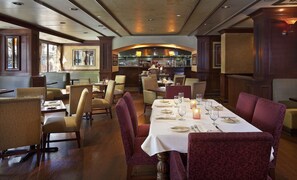 A restaurant with a central dining area featuring a long table set for a meal, surrounded by upholstered chairs.