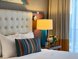 A hotel room with a tufted headboard, a bedside lamp, a floral arrangement, and a striped pillow.