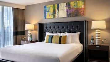 A hotel room with a large bed, two bedside tables, a city view, and a colorful abstract painting above the bed.