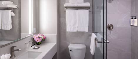 Un baño moderno con cabina de ducha de vidrio, inodoro blanco y tocador con lavabo y espejo.