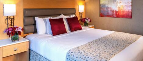 A neatly made bed with a patterned bedspread, two bedside tables with lamps, a vase of flowers, and a painting on the wall.
