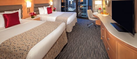 A hotel room with two beds, a desk, a TV, and a view of the city.