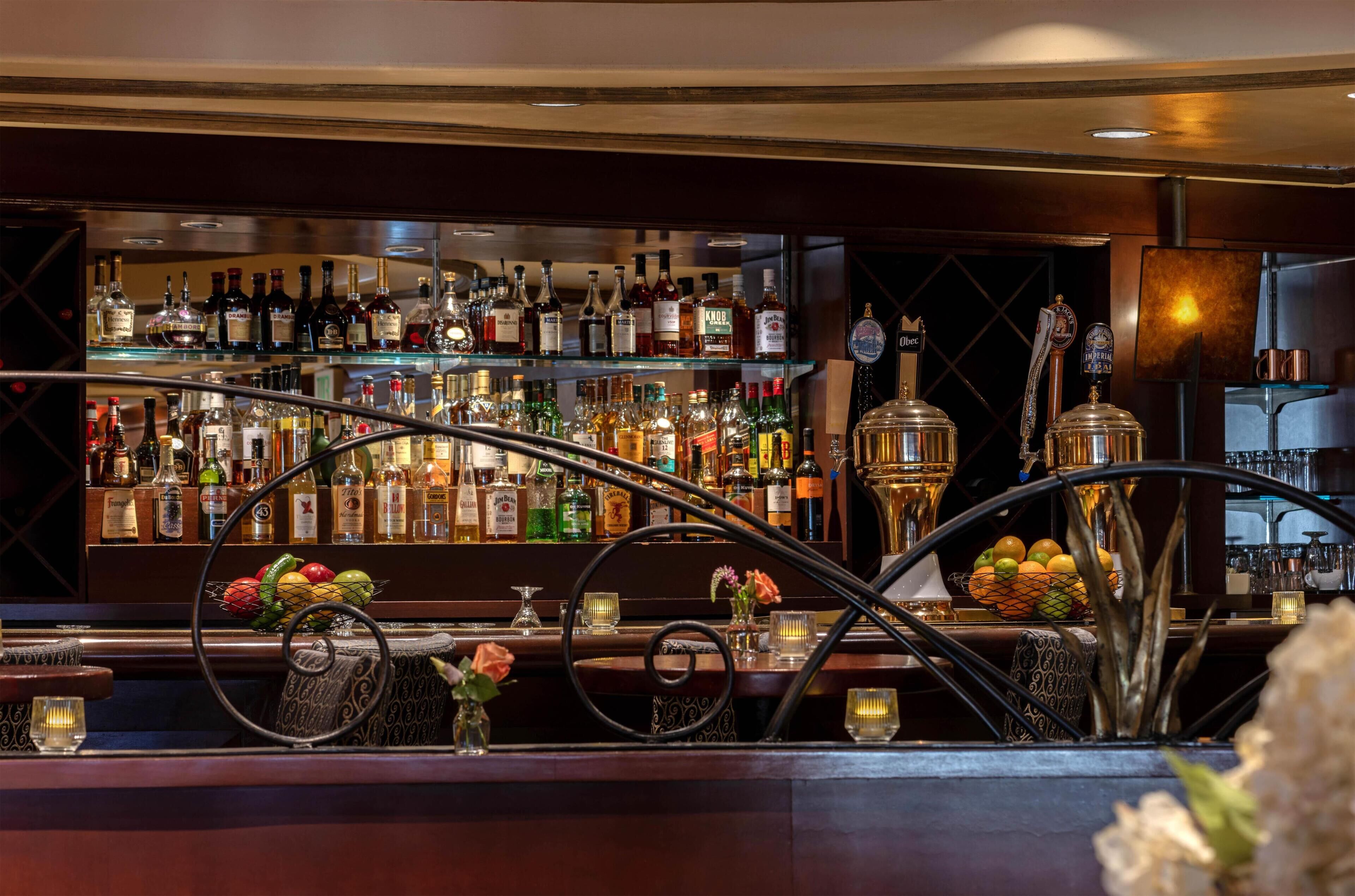 A bar area with a variety of liquor bottles, a fruit display, and a decorative metal arch.