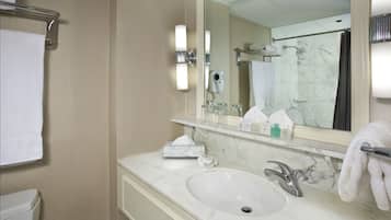 A hotel bathroom with a marble sink, a mirror, a towel rack, and a shower area.