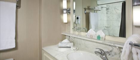 A hotel bathroom with a marble sink, a mirror, a towel rack, and a shower area.
