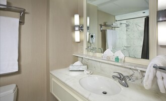A hotel bathroom with a marble sink, a mirror, a towel rack, and a shower area.