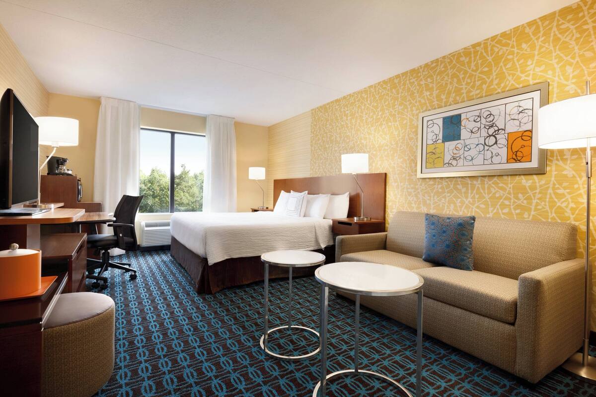 Ein Hotelzimmer mit Bett, Sofa, Schreibtisch mit Stuhl, Fernseher und Lampe.