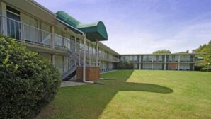 A modern building with a covered outdoor area, a grassy lawn, and a staircase leading to the entrance. - Express Airport Inn (Sandston)