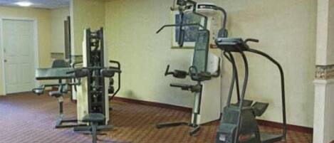 A fitness room with cardio and strength equipment, carpeted floor, and a door in the background.