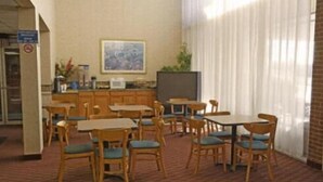 A dining area with wooden tables and chairs, a television, and a painting on the wall. - Express Airport Inn (Sandston)