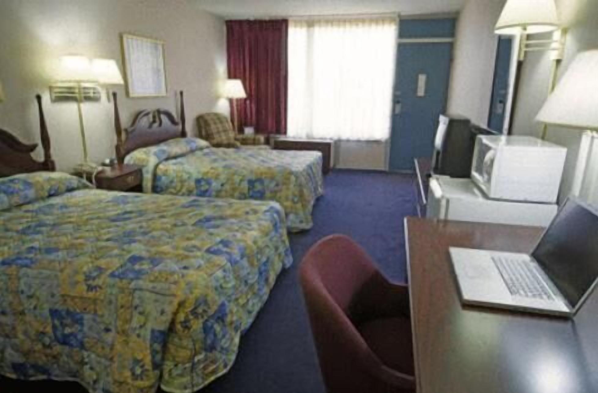 Une chambre d’hôtel avec deux lits, un bureau avec un ordinateur portable, une chaise, une télévision et une fenêtre avec des rideaux.