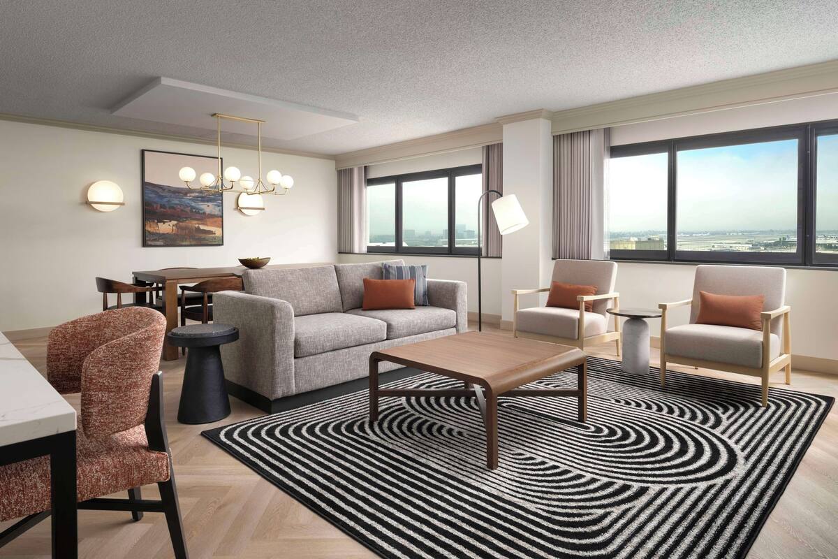 A modern living room with a sofa, armchairs, a coffee table, and a dining area with a table and chairs.