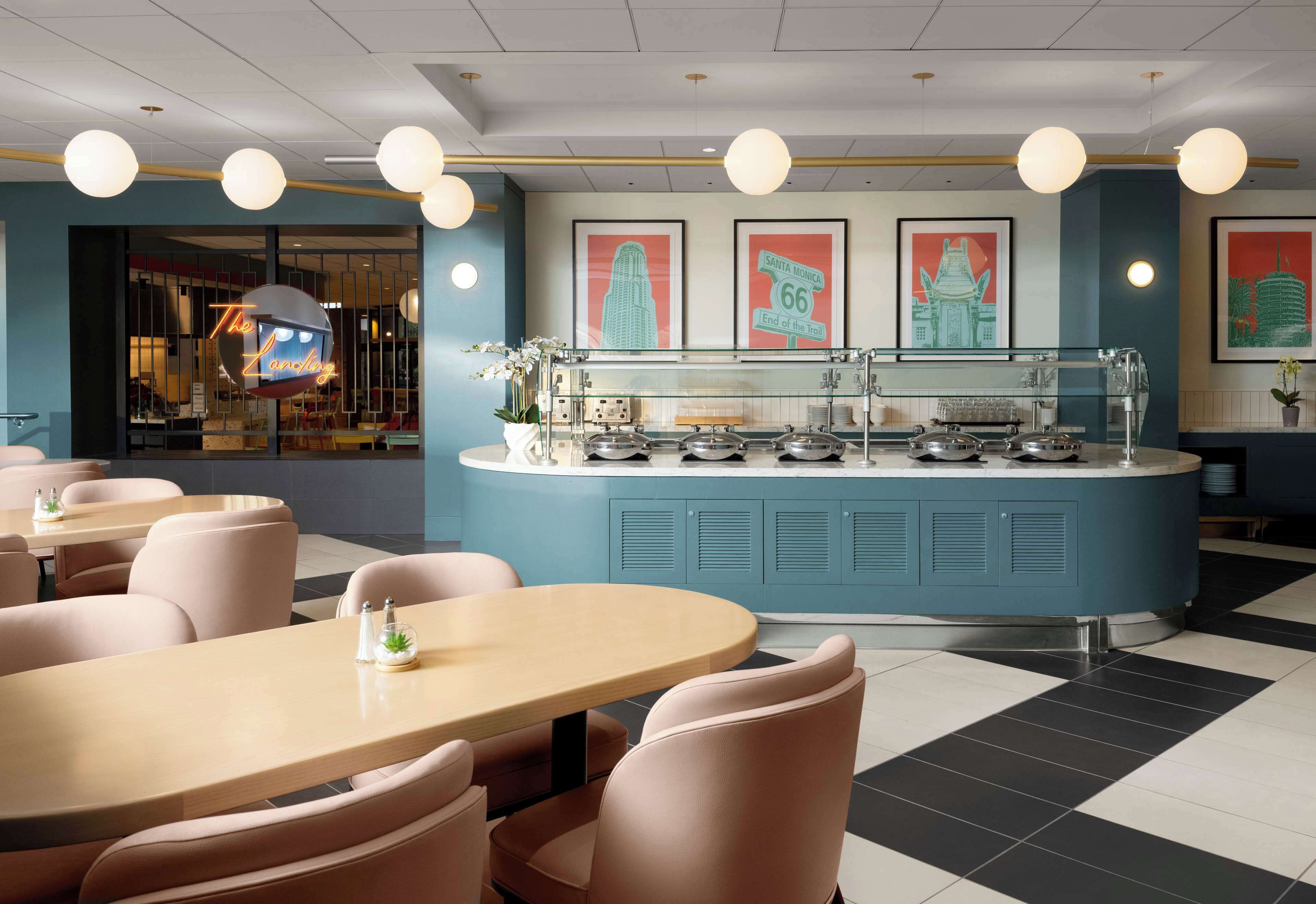 A modern restaurant with a central counter, seating area with round tables and chairs, and wall-mounted light fixtures.