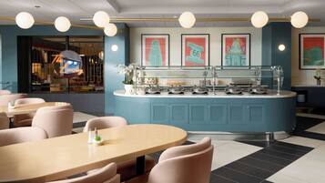 A modern restaurant with a central counter, seating area with round tables and chairs, and wall-mounted light fixtures.
