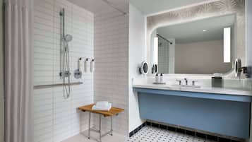 Un baño moderno con ducha, tocador con espejo y un taburete pequeño.